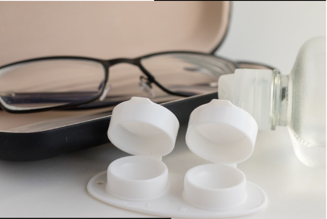 a pair of reading glasses next to a contact lens case with a bottle of solution